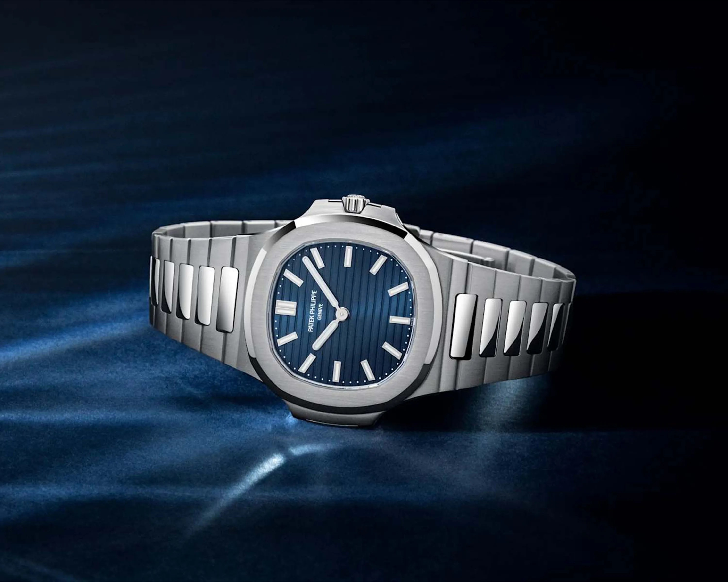 Silver stainless steel Patek Philippe wristwatch with a blue textured dial on a dark blue surface.