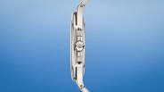 Side view of a slim silver metal wristwatch with a detailed crown and integrated lugs on a gradient blue background.