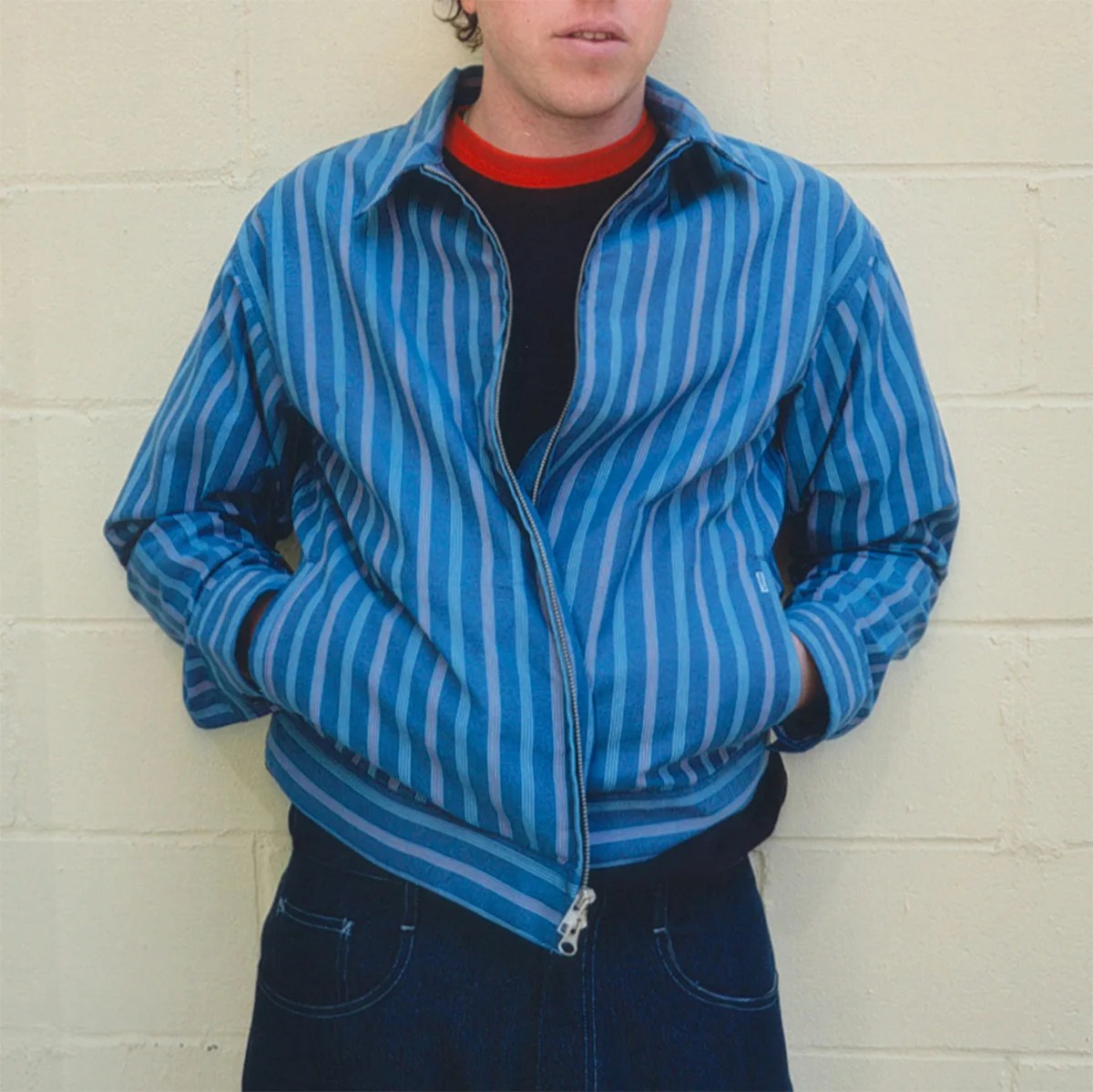 Blue and navy striped zip-up jacket worn over a black shirt with a red collar.