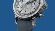 Close-up of a silver chronograph watch with blue hands, textured dial, and blue leather strap against a blue background.