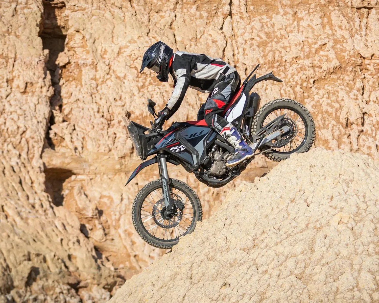 Person wearing black, white, and red riding gear on a black and gray off-road motorcycle climbing a rocky hill.