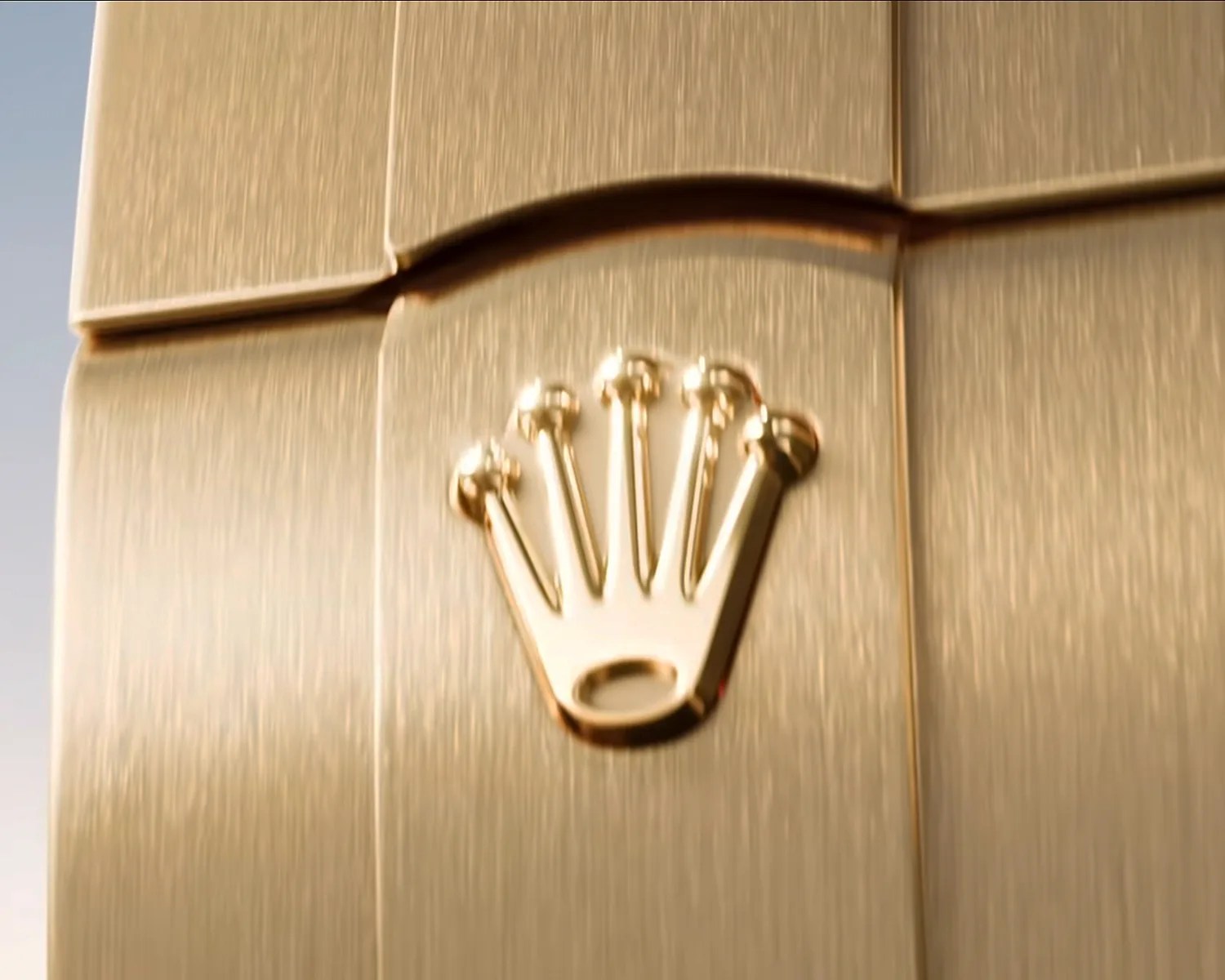 Close-up of a gold Rolex watch bracelet with the Rolex crown logo embossed on a brushed metal link.