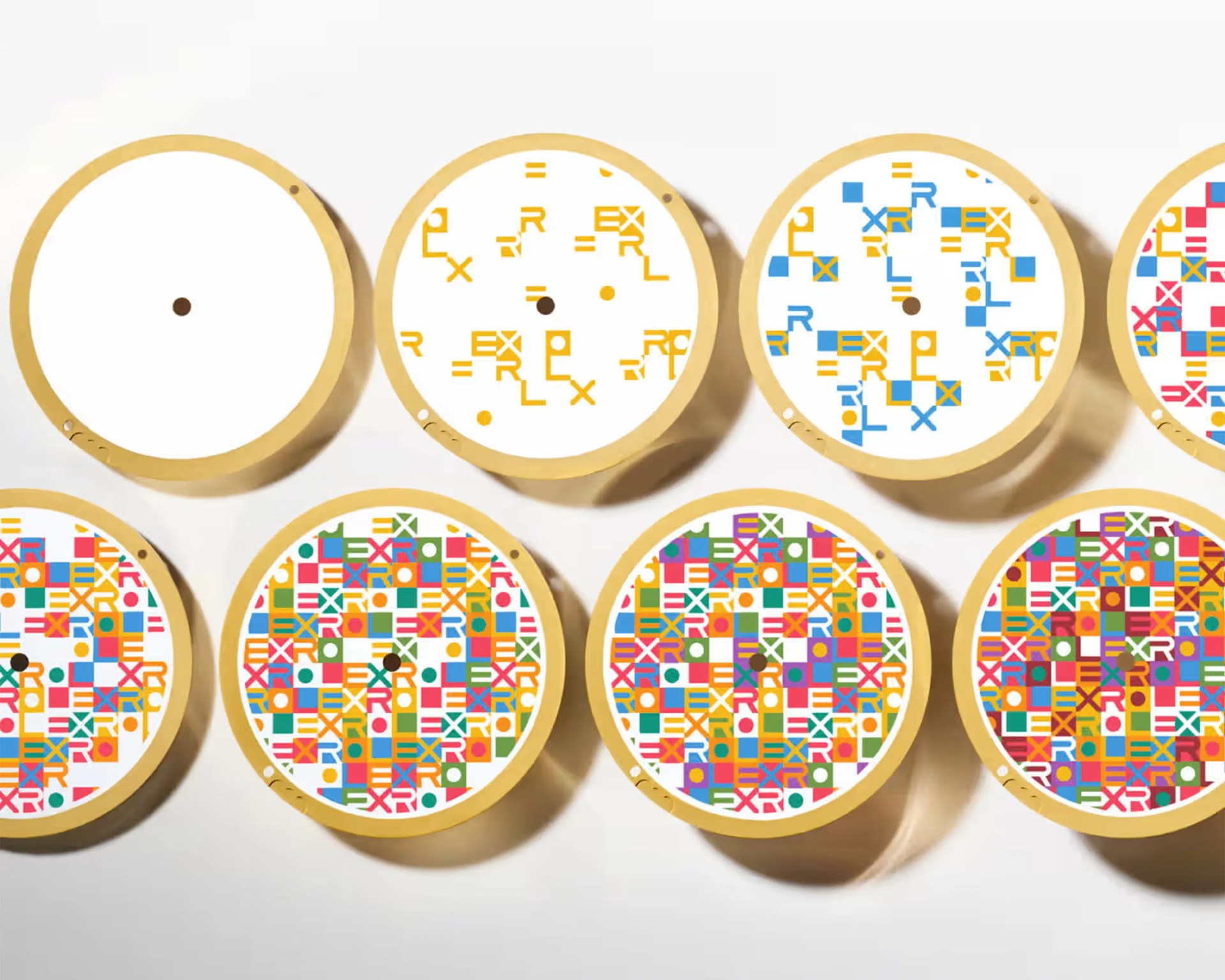 Ten round wooden embroidery hoops with white fabric, each showing a different stage of a colorful geometric pattern with letters and shapes.