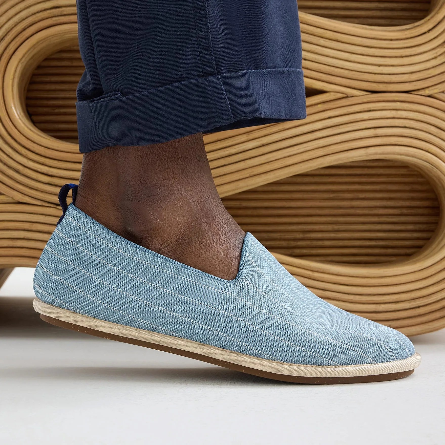 Light blue slip-on shoe with white stripes and beige sole worn with navy pants.