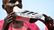 White Adidas running shoe with black stripes and handwritten text "1:59.30 WR sub 2" held by a person in a pink jacket.