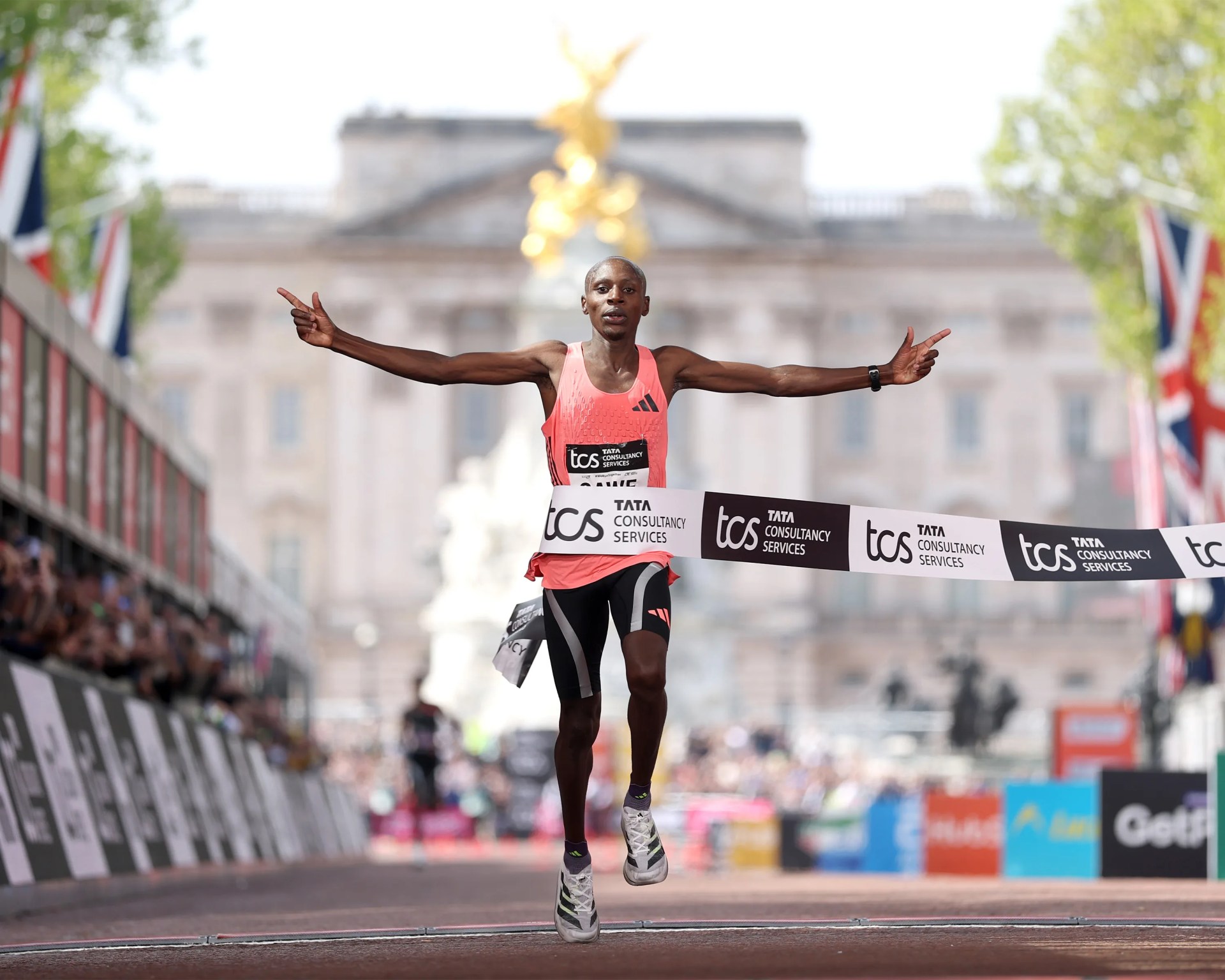 Runner in a pink Adidas tank top crossing the finish line at a marathon with arms outstretched.