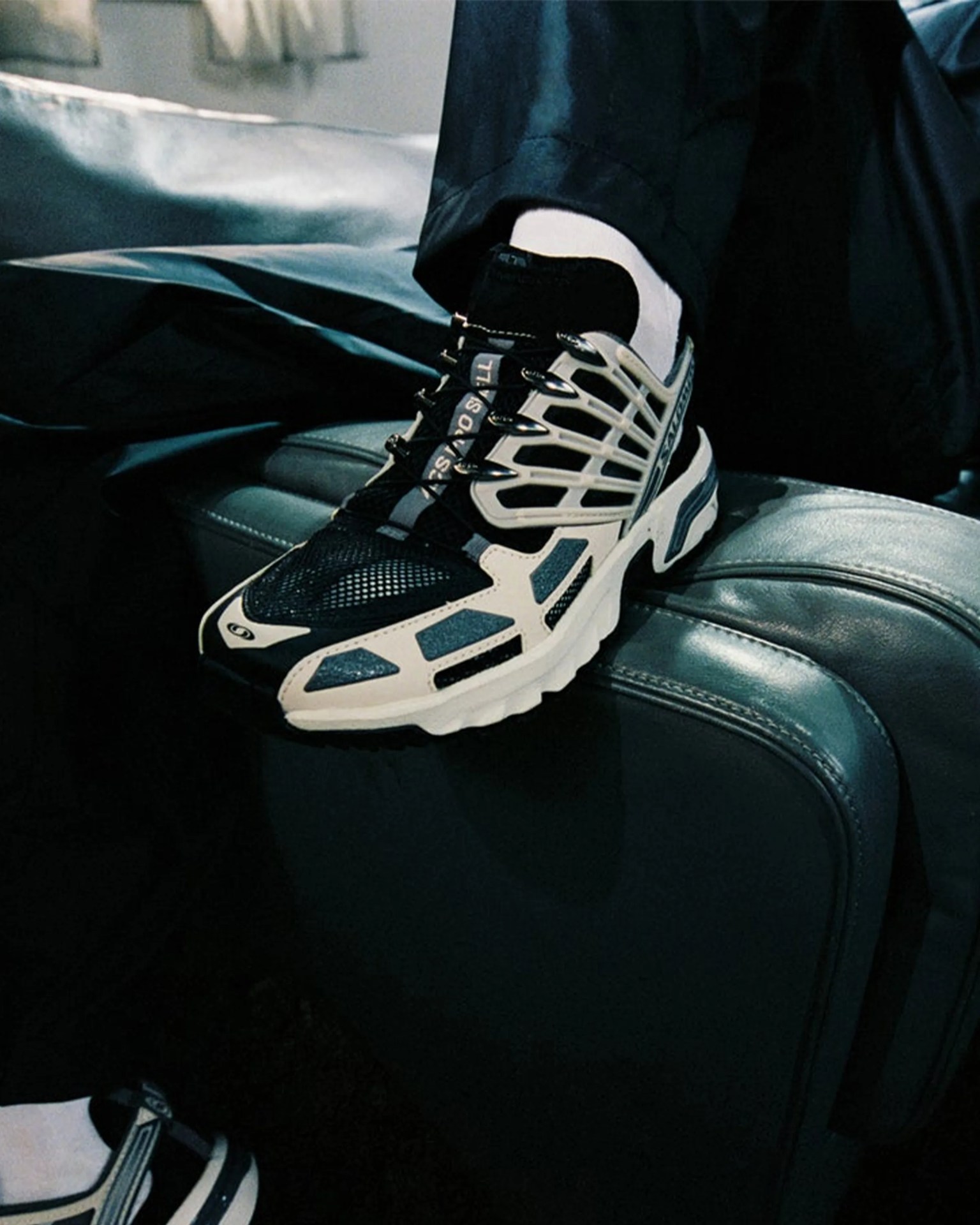 Black and white mesh athletic sneaker with cage-like overlays worn with white socks and black pants.