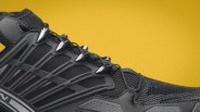 Close-up of a black athletic shoe with mesh and synthetic overlays against a yellow background.
