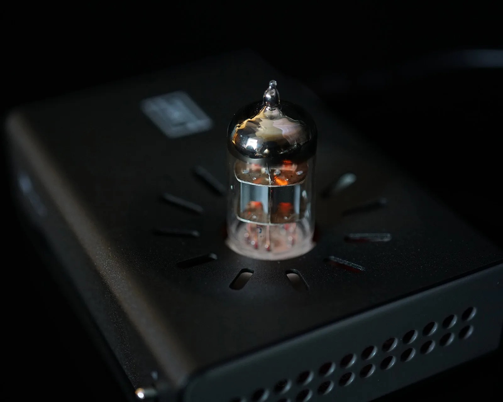 Glass vacuum tube with a reflective silver top mounted on a black perforated electronic device.