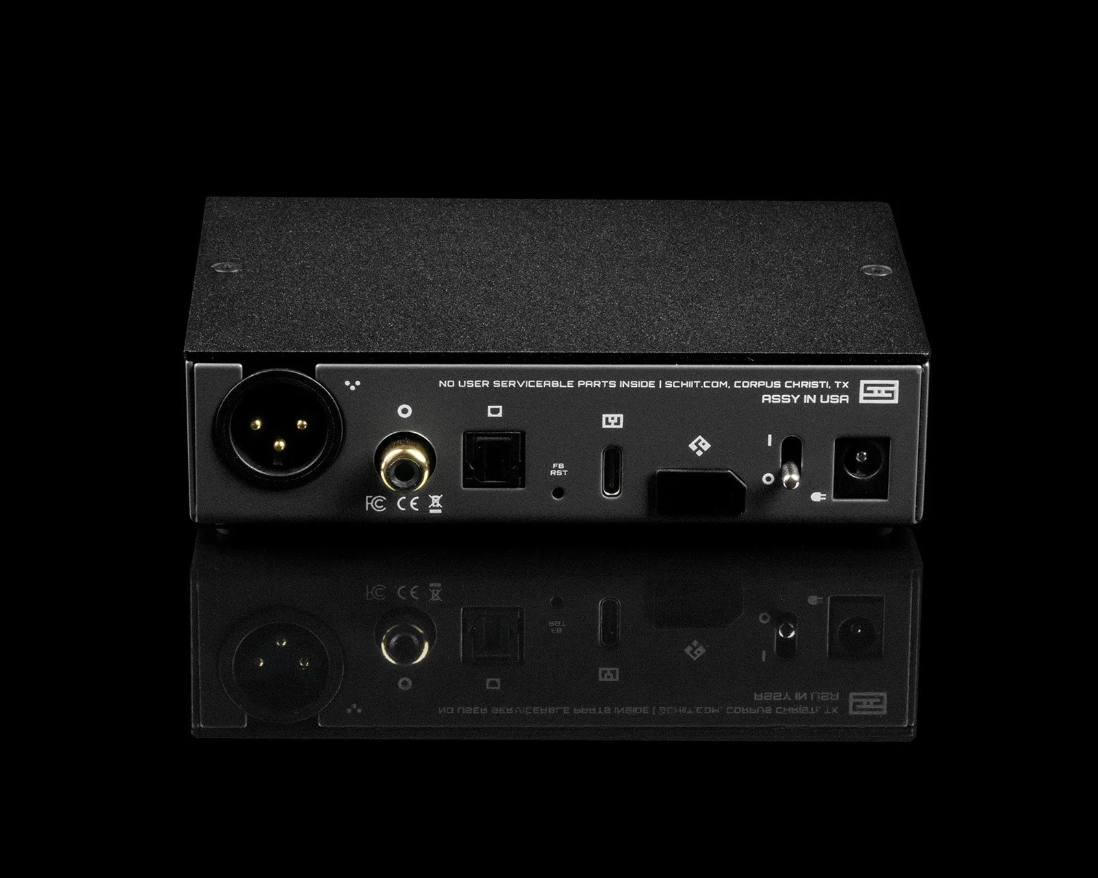 Black rectangular audio device with various input/output ports and a power switch on a reflective black surface.