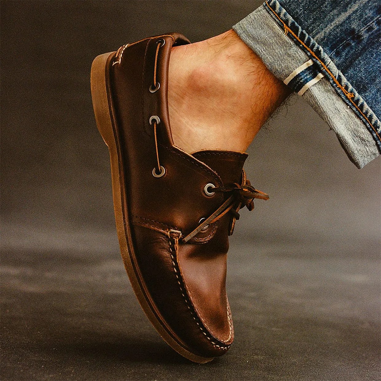 Brown leather boat shoe with laces worn with cuffed blue denim jeans.
