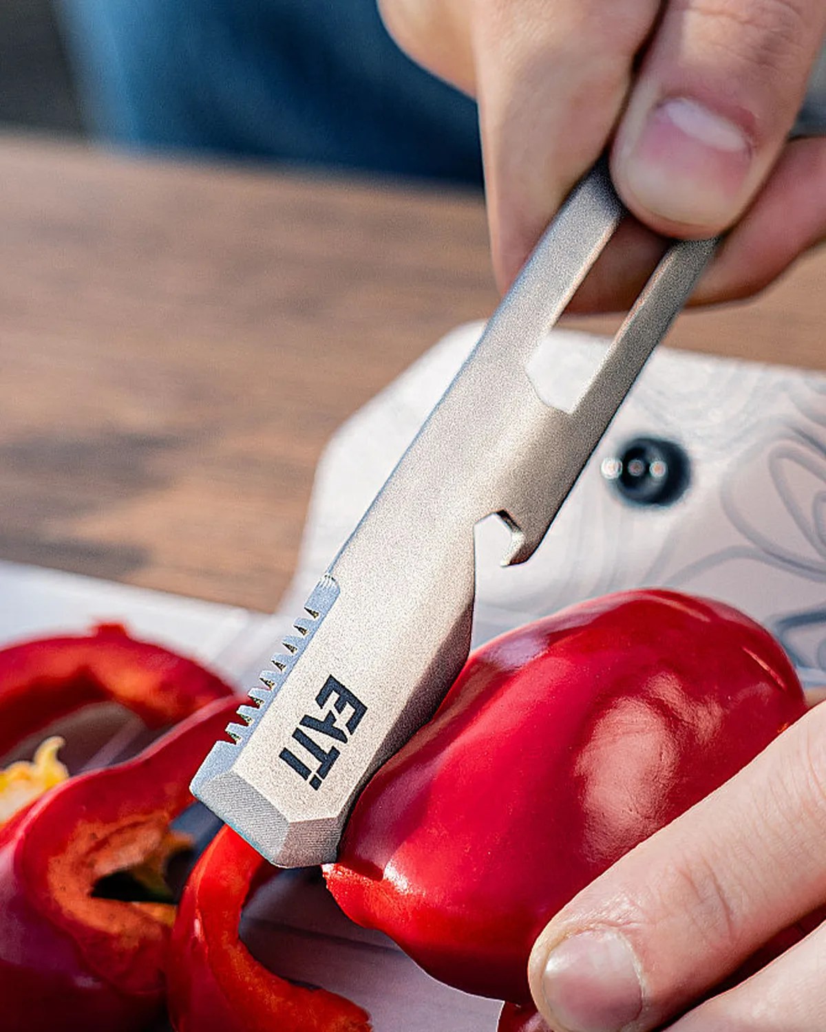 Silver multi-tool with "ETTI" logo cutting a red bell pepper on a wooden surface.