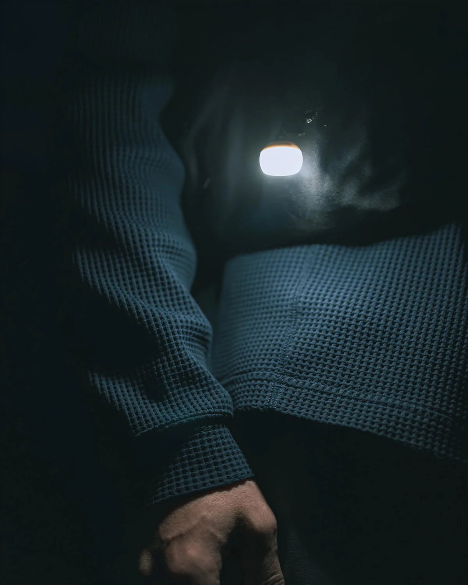 Hand holding a small, bright, round light source in a dark setting with a textured dark blue sleeve.