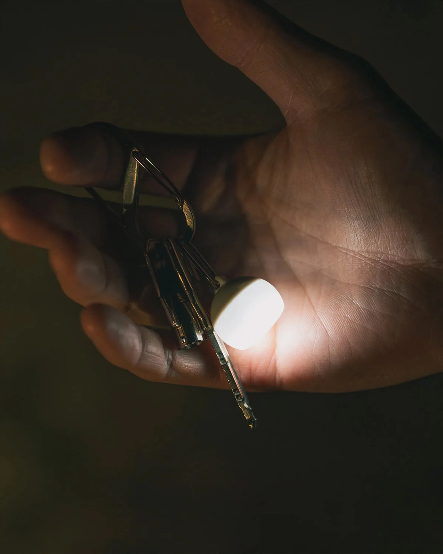 Hand holding a set of metallic keys with a glowing white keychain light in a dark setting.