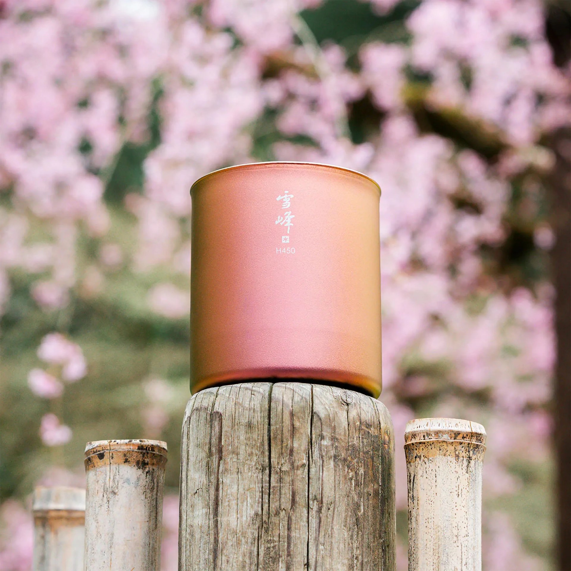 Matte copper-colored cylindrical container with white Asian characters and "H450" text, placed on weathered wooden post.