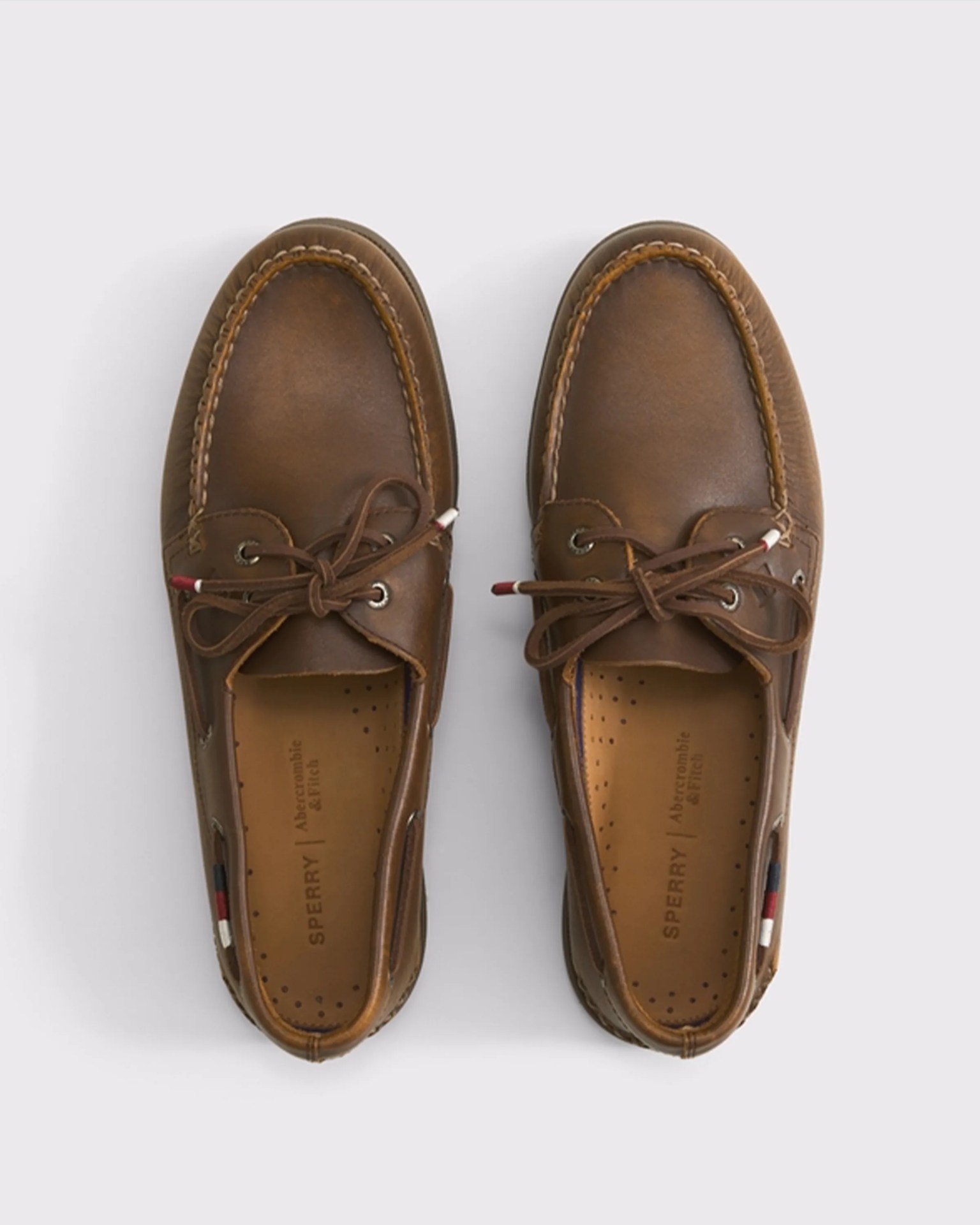 Pair of brown leather Sperry boat shoes with laces tied in bows, viewed from above on a light background.