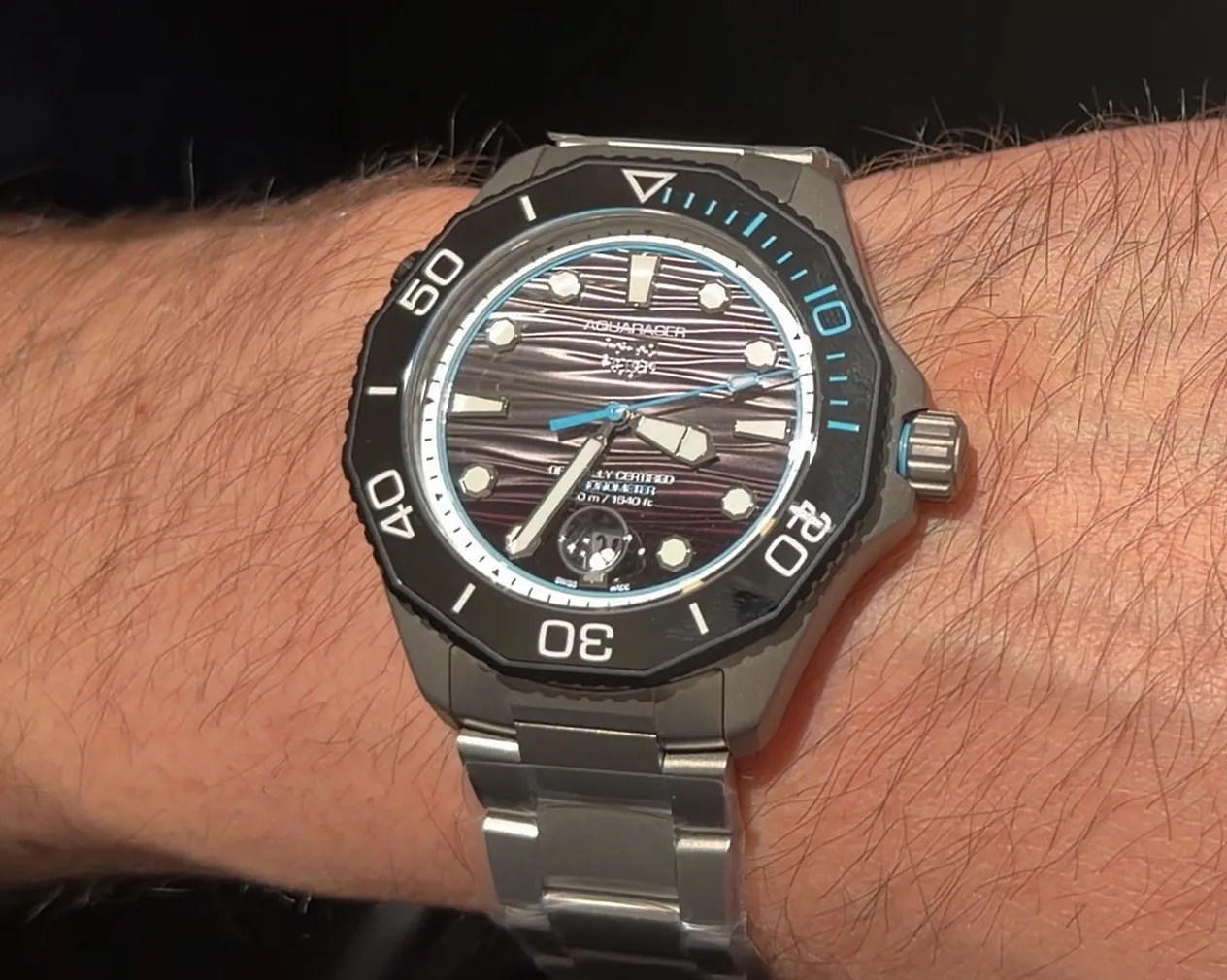 Silver metal bracelet watch with black bezel and textured dark dial worn on a wrist.