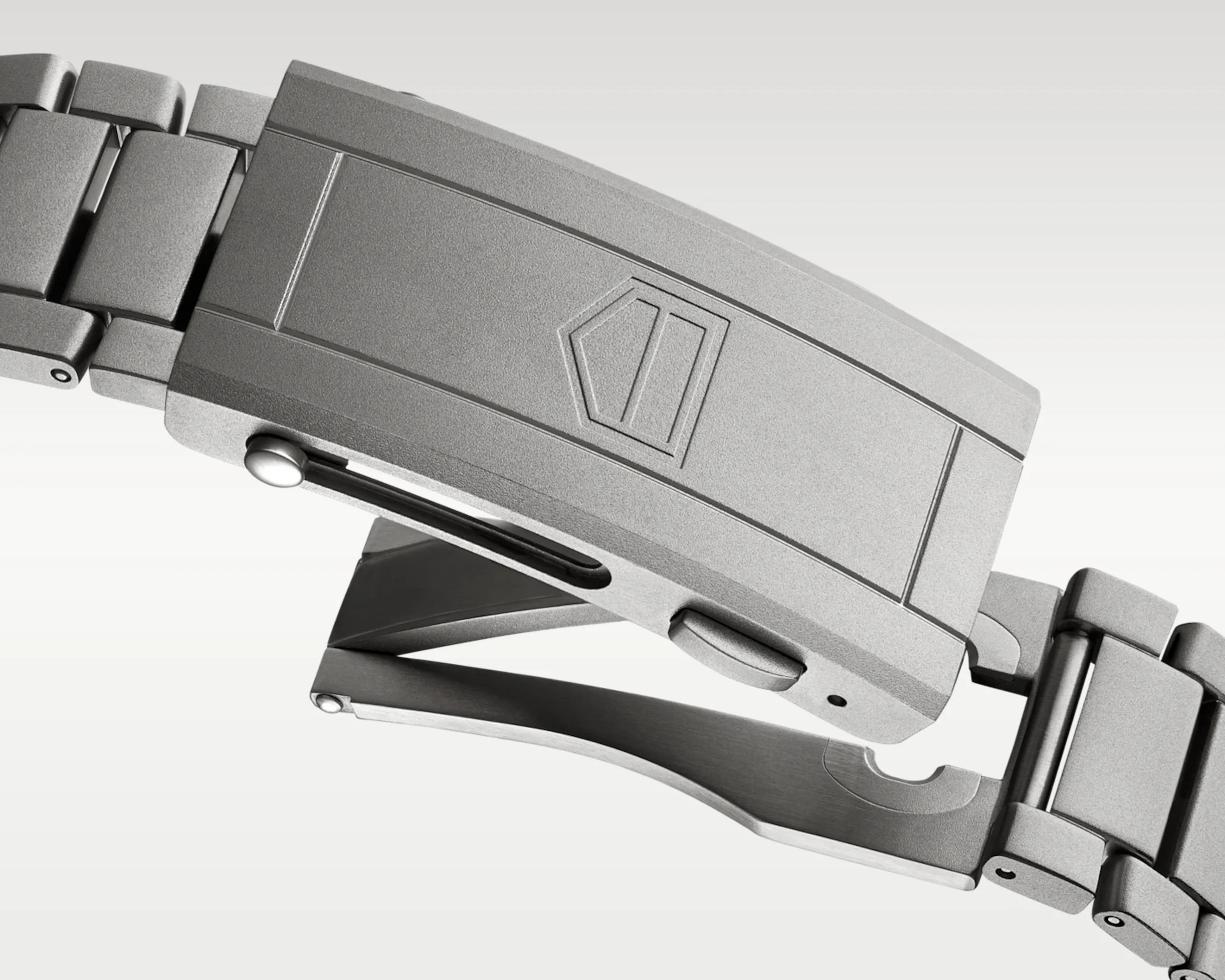 Matte silver metal watch clasp with a pentagon-shaped logo and linked bracelet segments.