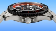 Silver TAG Heuer Aquaracer watch with black and orange bezel and textured dial, side view on blue background.