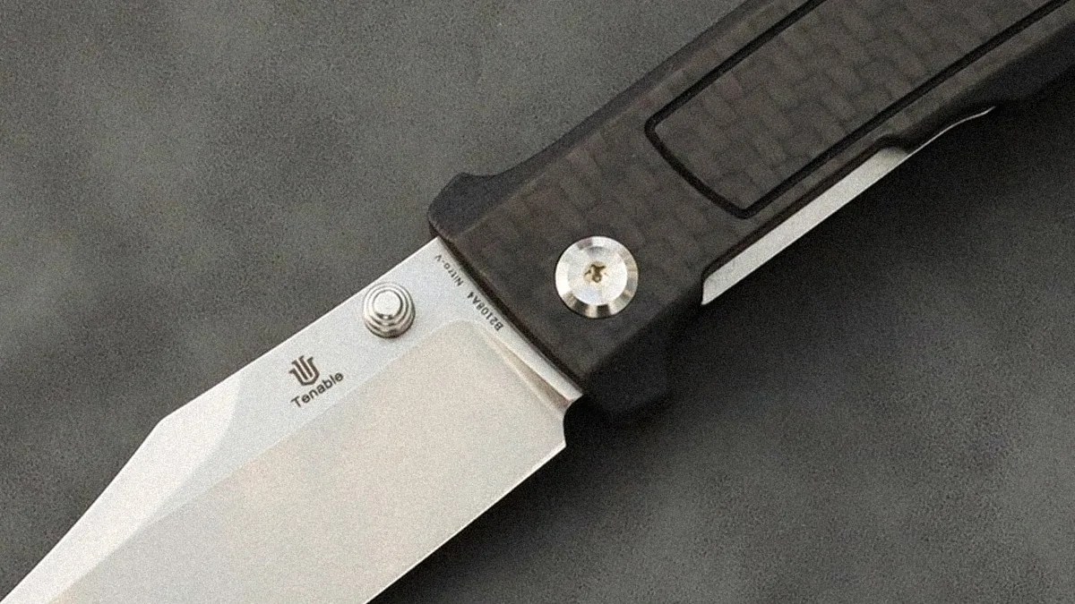 Close-up of a folding knife with a silver blade marked "Tenable" and a dark textured handle.