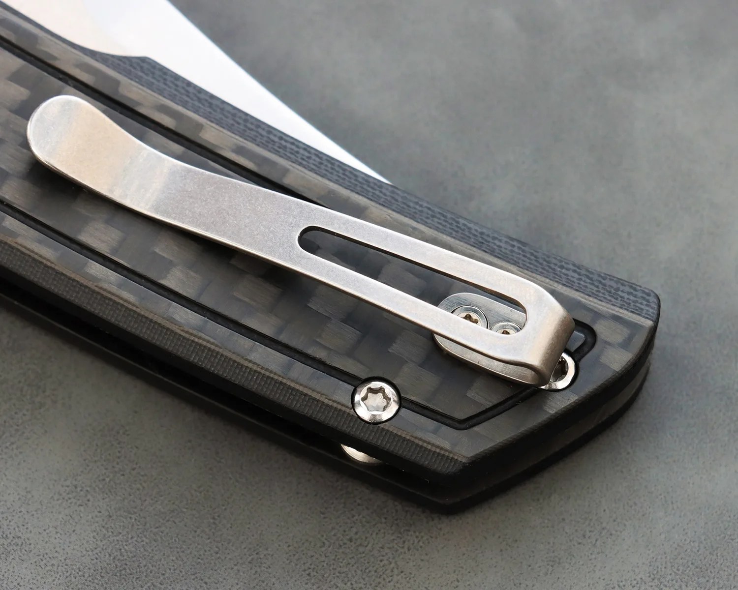 Close-up of a silver metal pocket clip attached to a black carbon fiber textured folding knife handle.