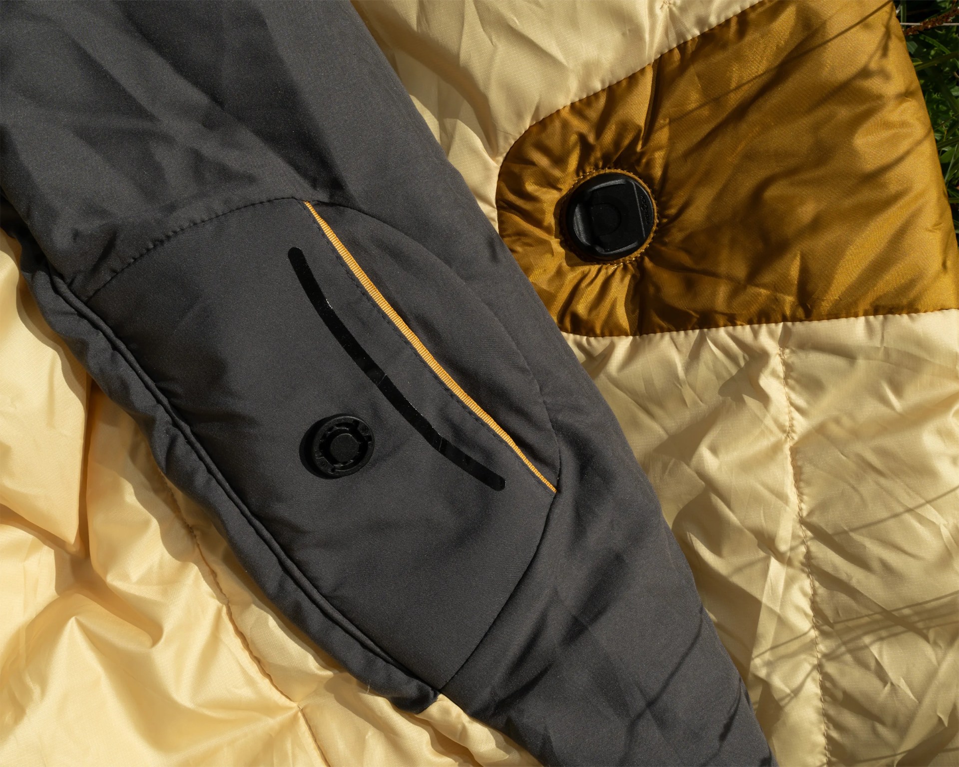 Close-up of a black jacket sleeve with a zippered pocket and a yellow and beige quilted fabric background.