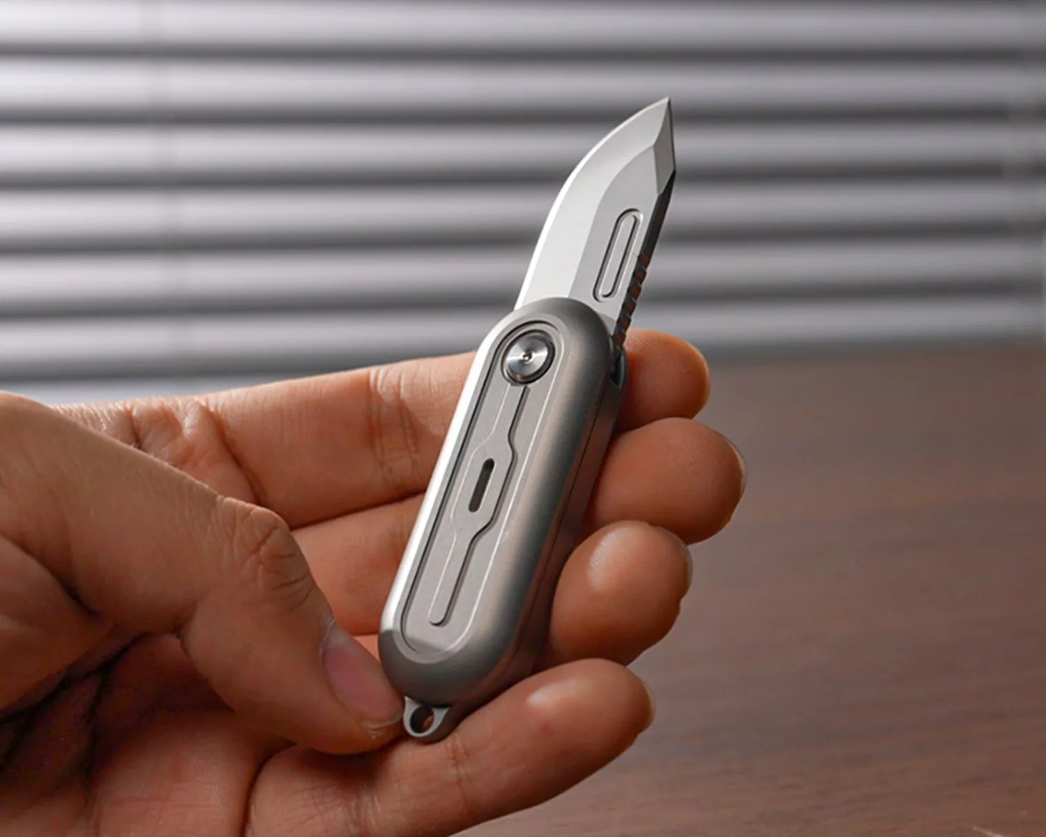 Hand holding a small silver folding knife with a partially serrated blade.