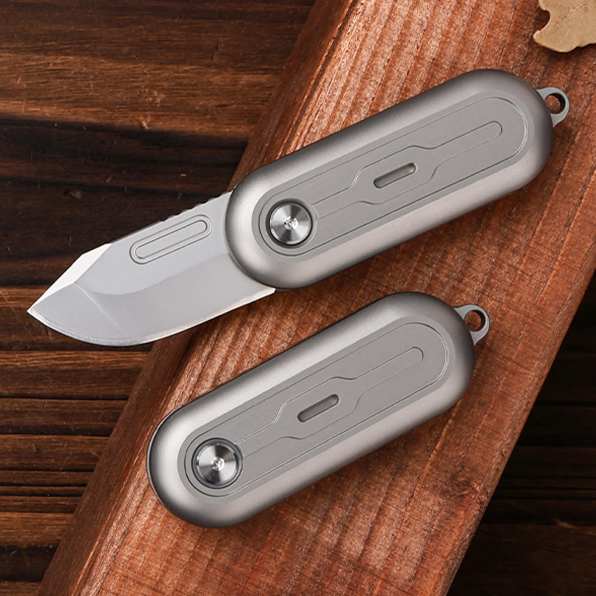 Silver folding knife with a rounded handle and a short, wide blade on a wooden surface.