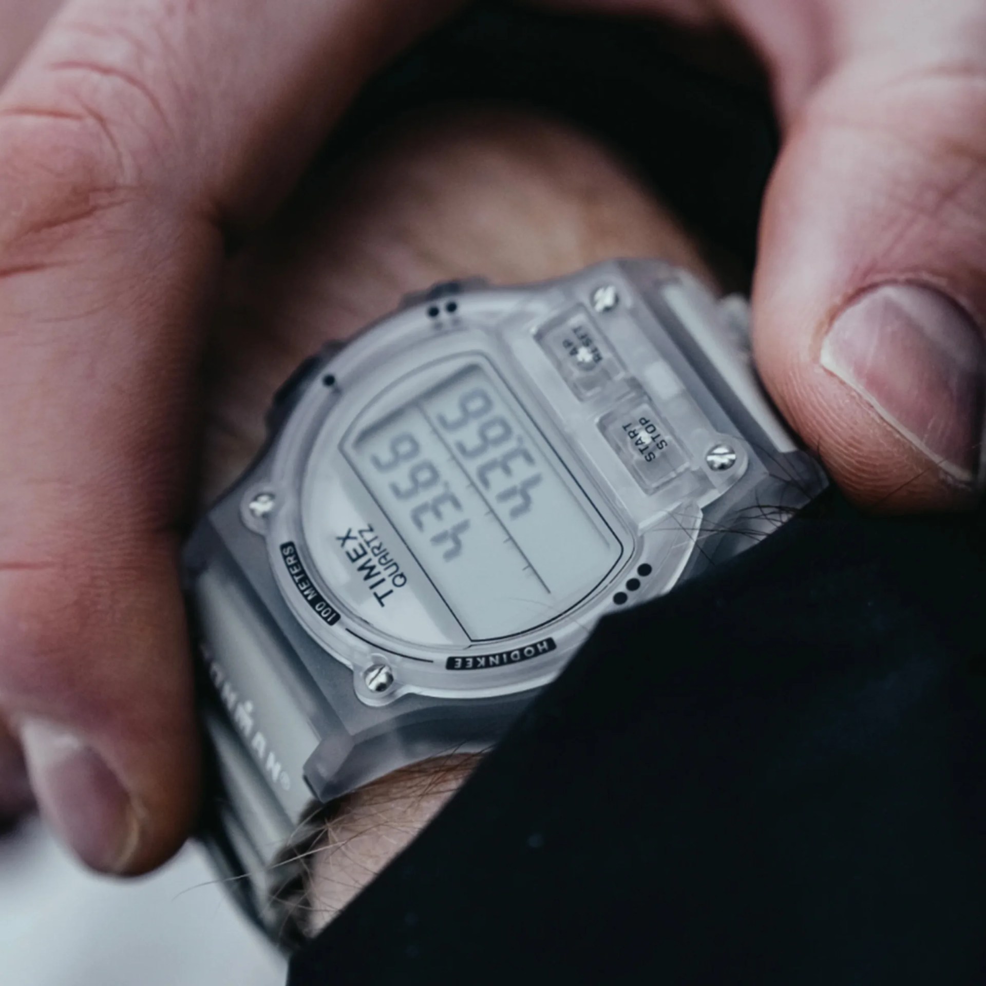 Close-up of a translucent Timex digital wristwatch with a gray strap worn on a wrist.