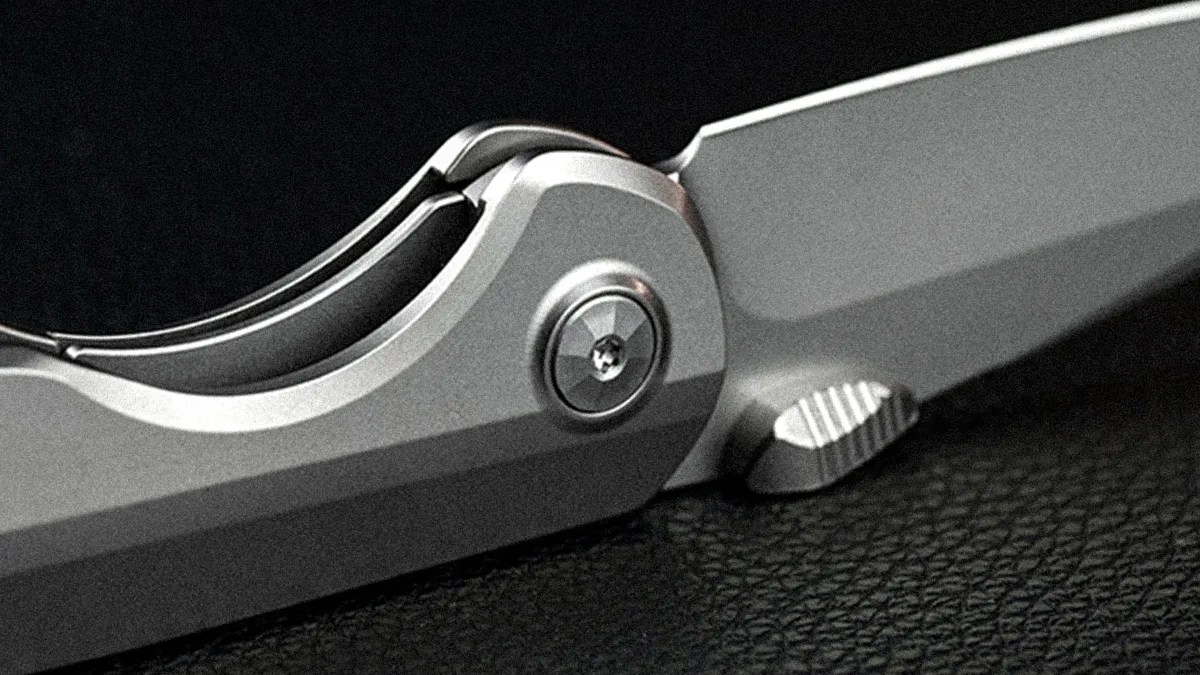Close-up of a silver folding knife with a textured thumb stud on a black textured surface.