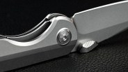 Close-up of a silver folding knife with a textured thumb stud on a black textured surface.