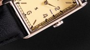 Close-up of a rectangular watch with a cream dial, silver hour markers, and a black leather strap.