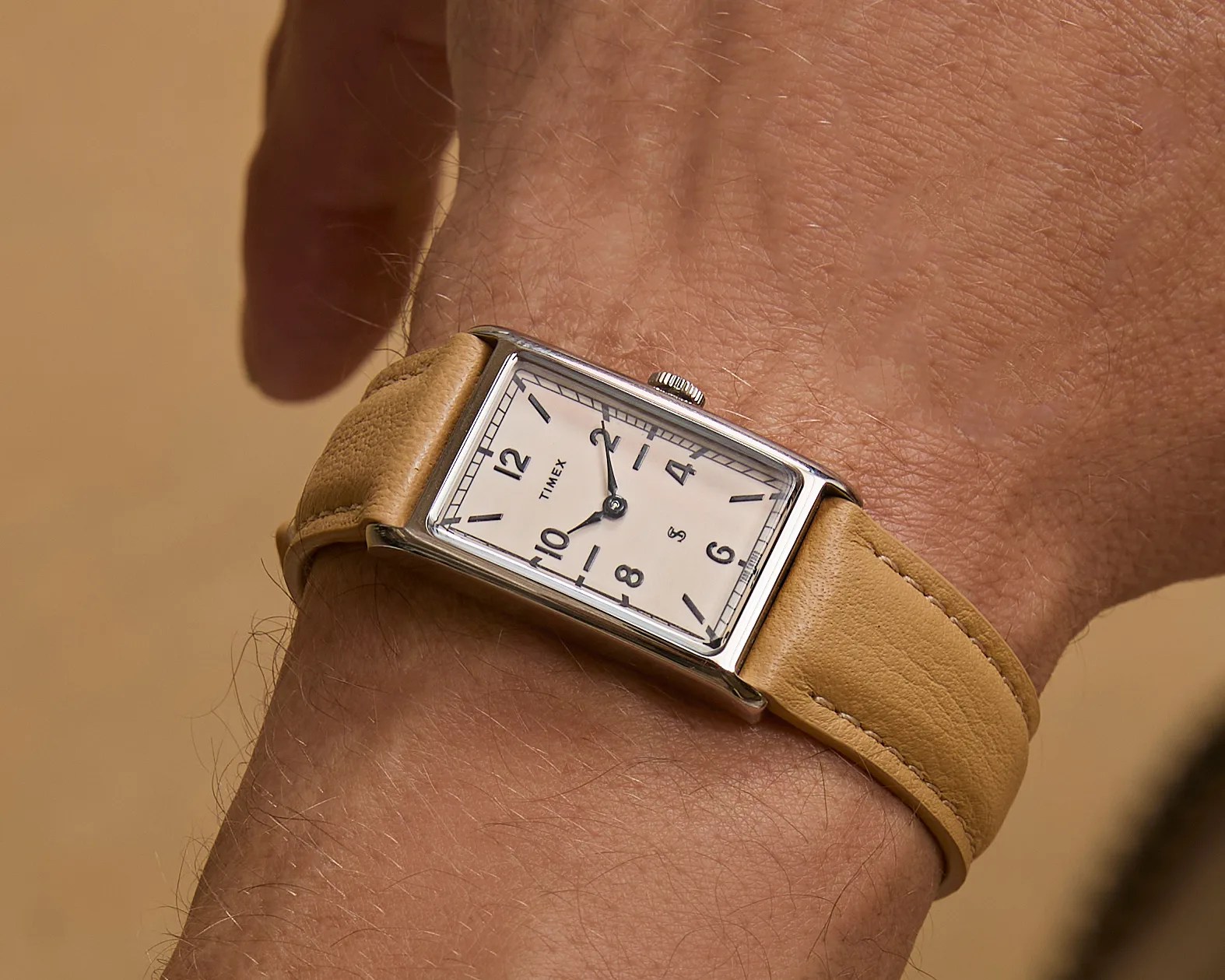 Rectangular silver Timex wristwatch with cream dial and tan leather strap worn on a wrist.