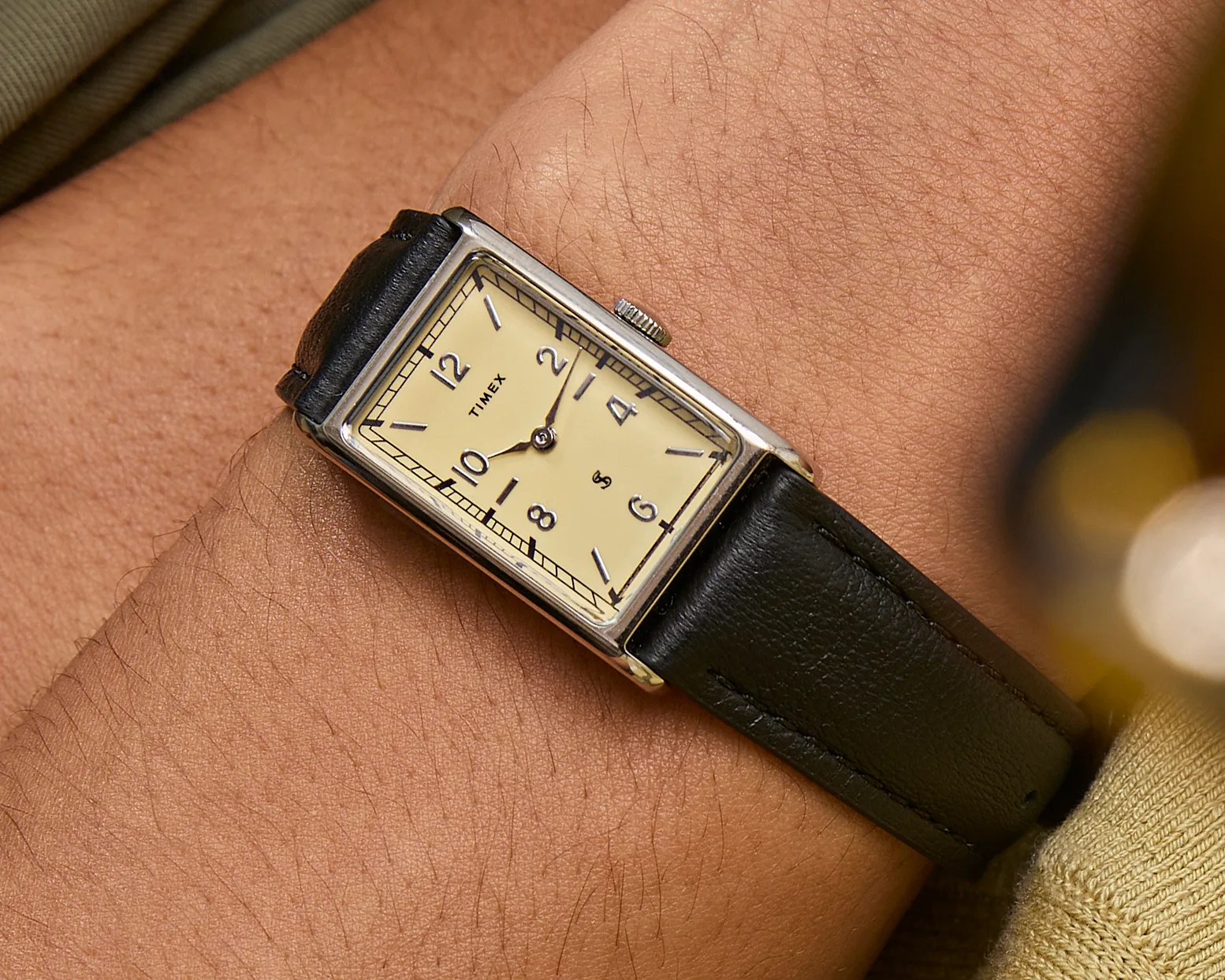 Rectangular silver Timex wristwatch with cream dial and black leather strap on a wrist.
