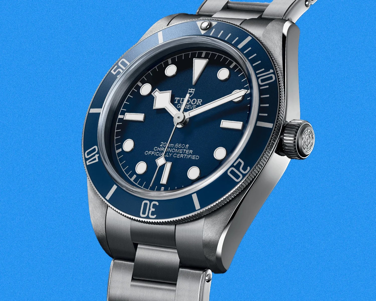 Stainless steel Tudor dive watch with blue bezel and dial, luminous markers, and metal bracelet on blue background.