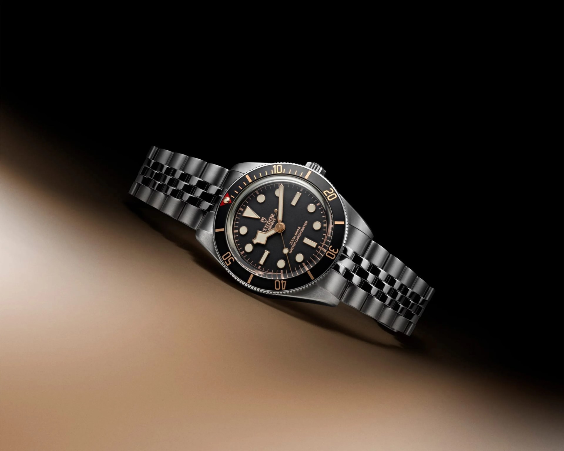 Stainless steel Tudor Black Bay wristwatch with black dial, gold-tone markers, and rotating bezel on a metal bracelet.