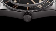 Close-up of a black watch crown with an engraved rose emblem and a black bezel with gold markings.