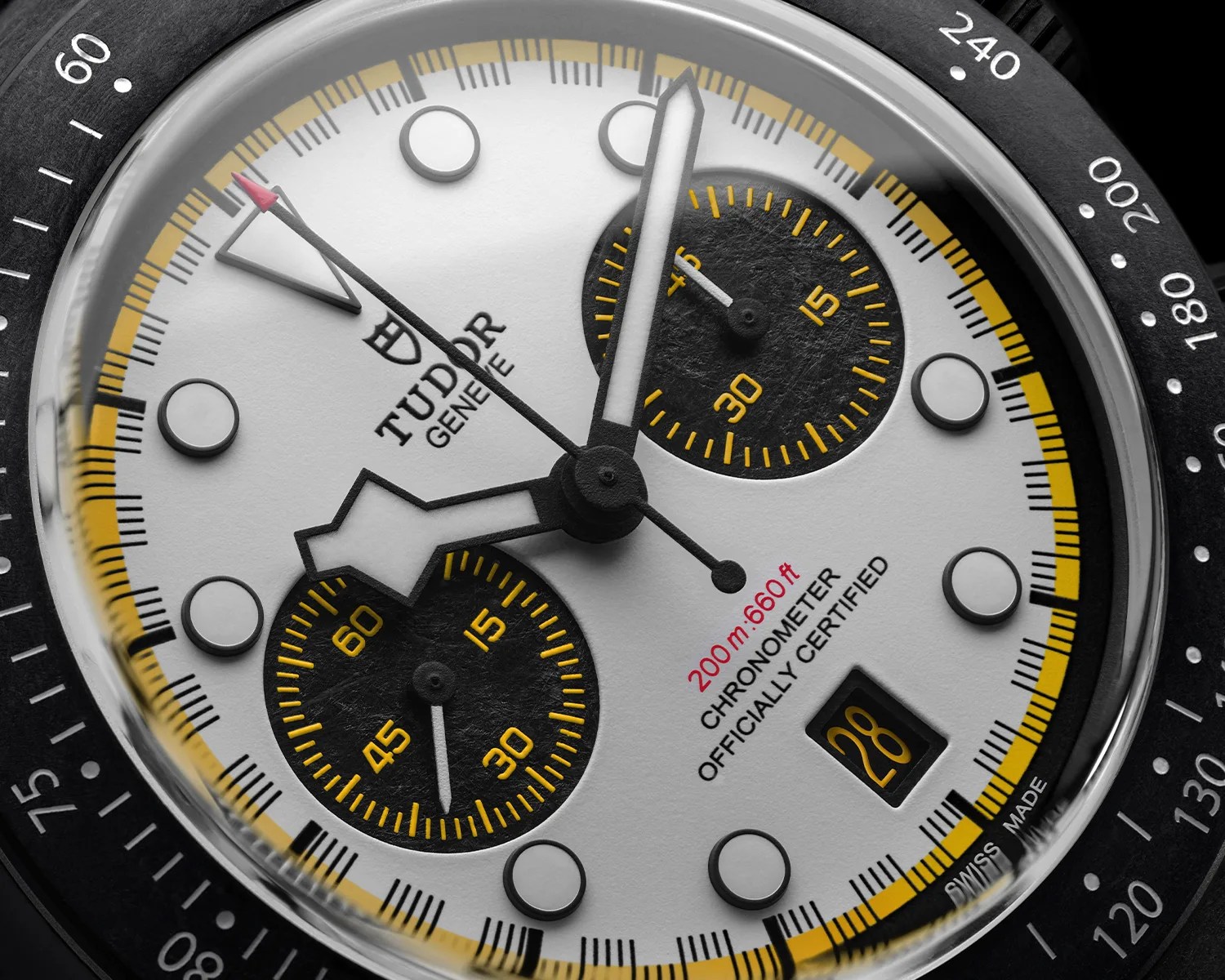 Close-up of a Tudor chronometer watch face with black subdials, yellow accents, and a date window showing 28.