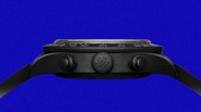 Side view of a black wristwatch with three textured crowns and a black strap against a blue background.