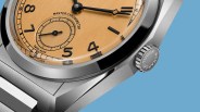 Close-up of a Tudor Monarch watch with a brushed orange dial, black numerals, and a stainless steel case and crown.