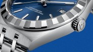 Close-up of a stainless steel watch with a blue dial, fluted bezel, date window at 3 o'clock, and a metal bracelet.