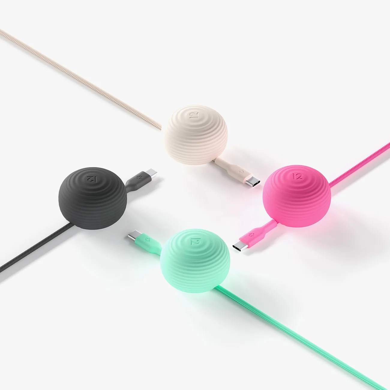 Four round, ribbed USB-C cables in black, beige, pink, and mint green with matching spherical cable organizers.
