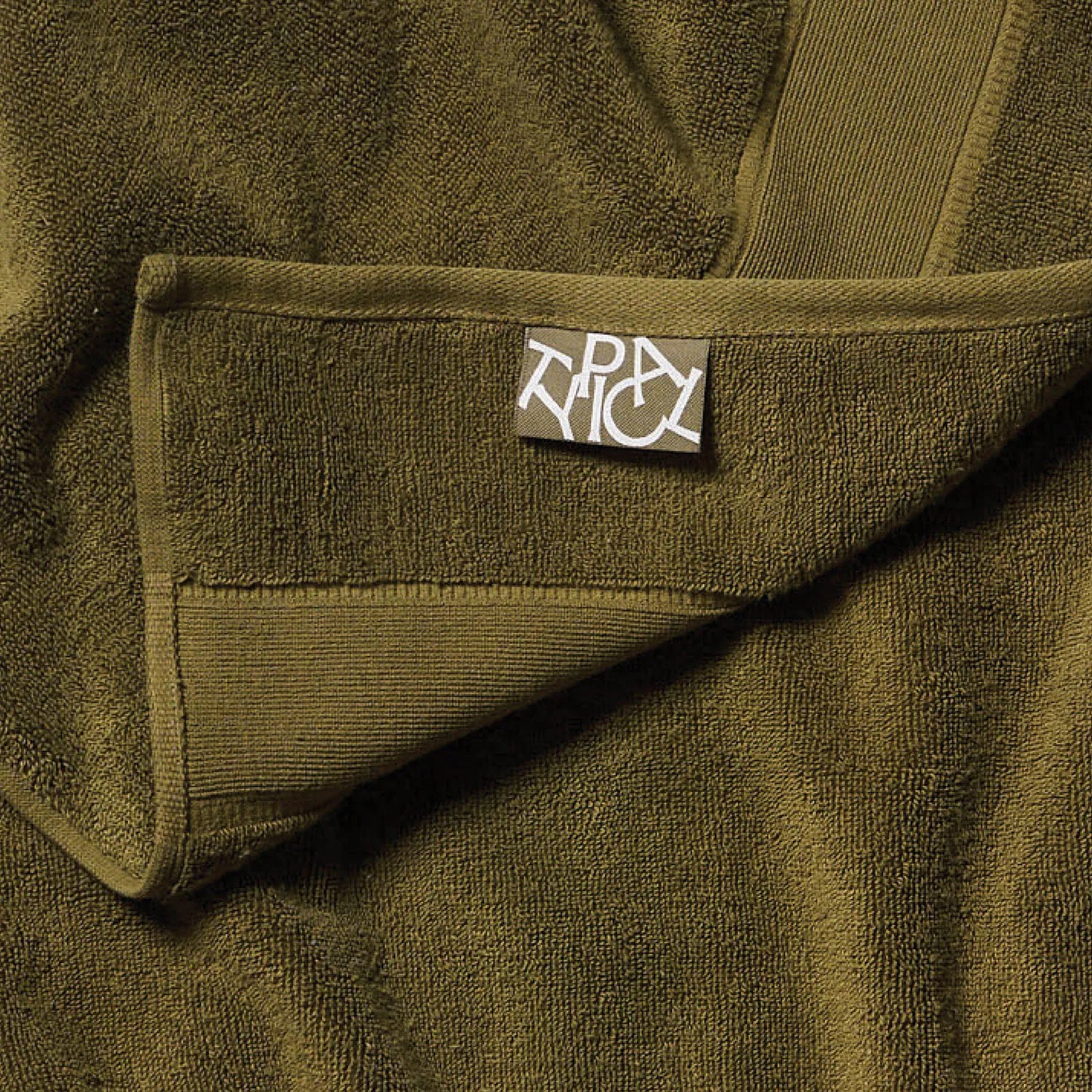Olive green terry cloth towel with a folded corner and a white abstract logo tag.