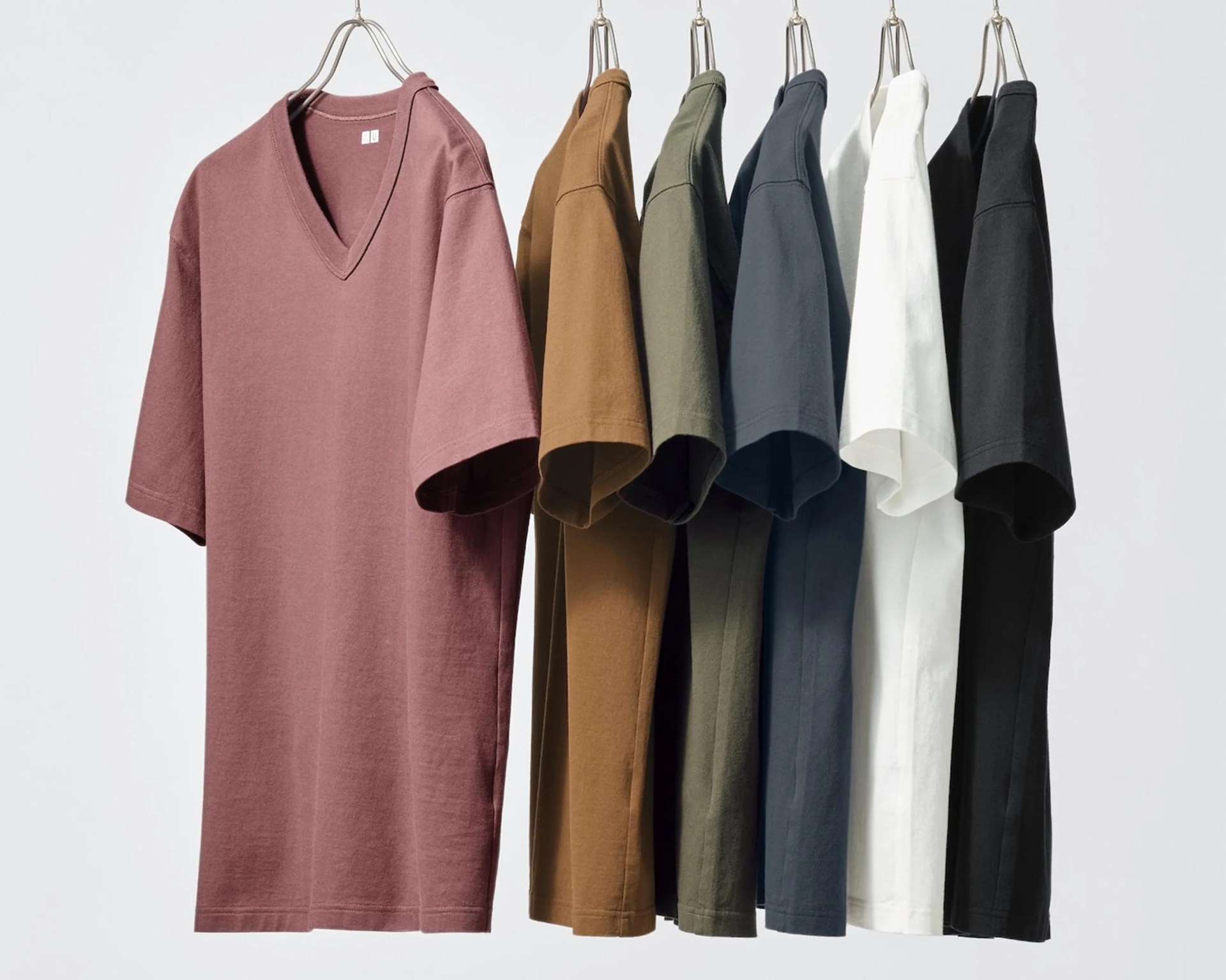 Seven short-sleeve V-neck t-shirts in mauve, brown, olive, navy, white, and black hanging on metal hangers.