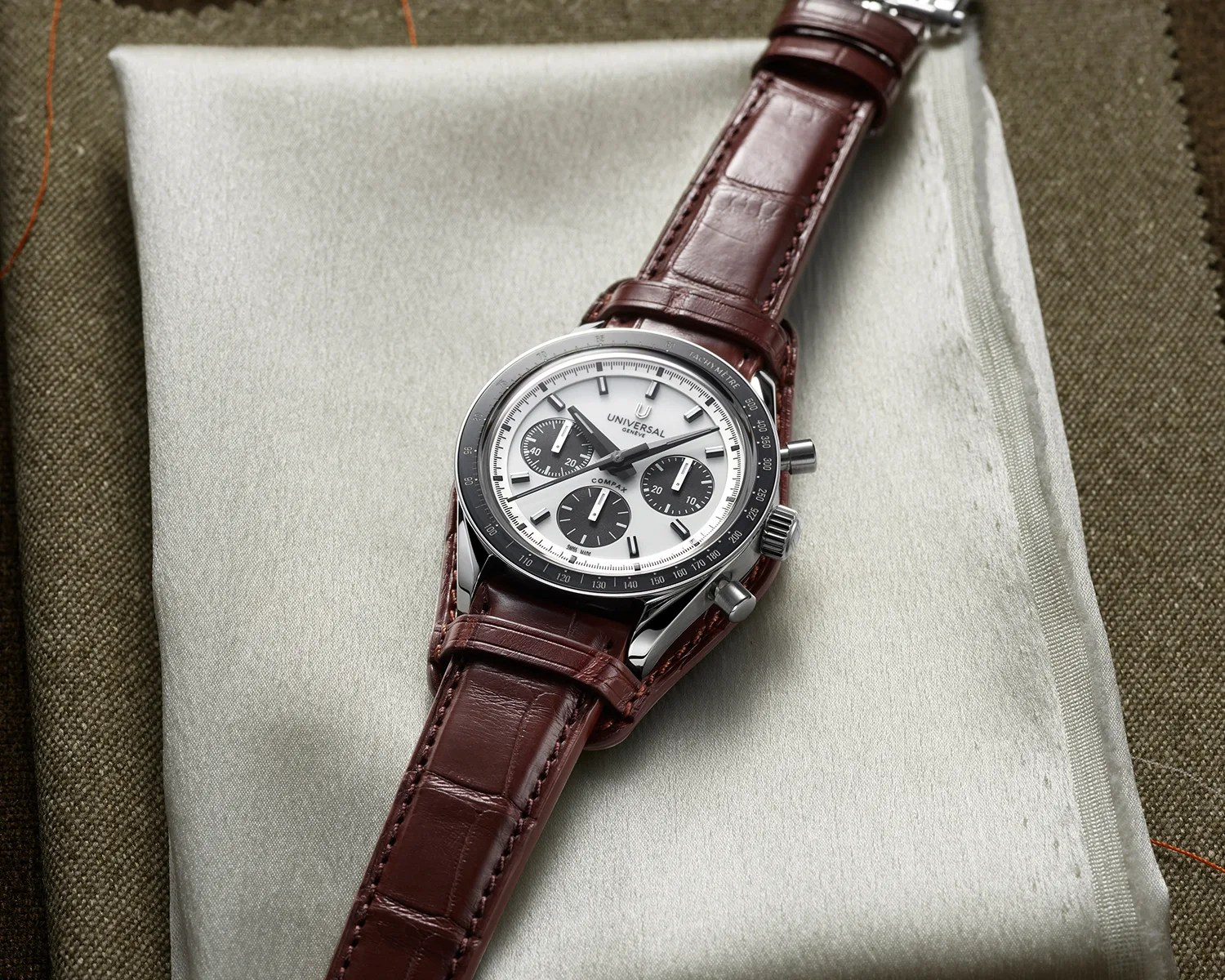 Silver Universal Gen&egrave;ve chronograph watch with white dial and black subdials on a brown leather strap.