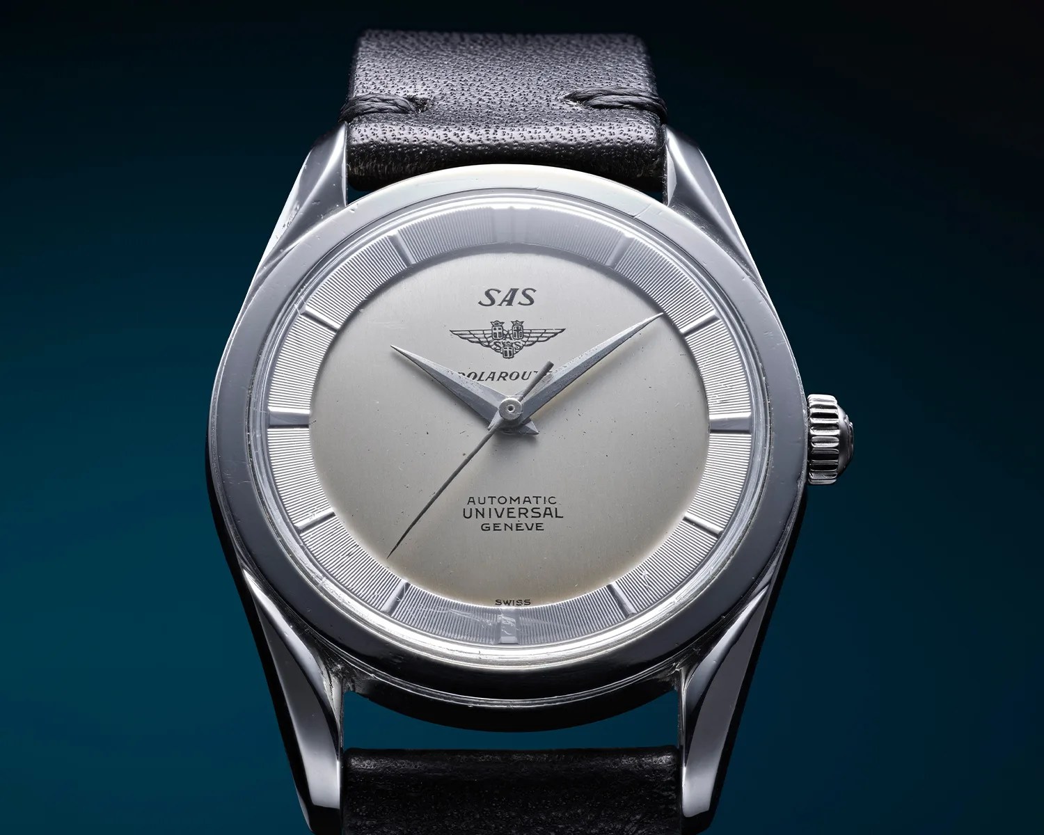 Silver Universal Gen&egrave;ve SAS Polerouter automatic wristwatch with black leather strap on a dark blue background.