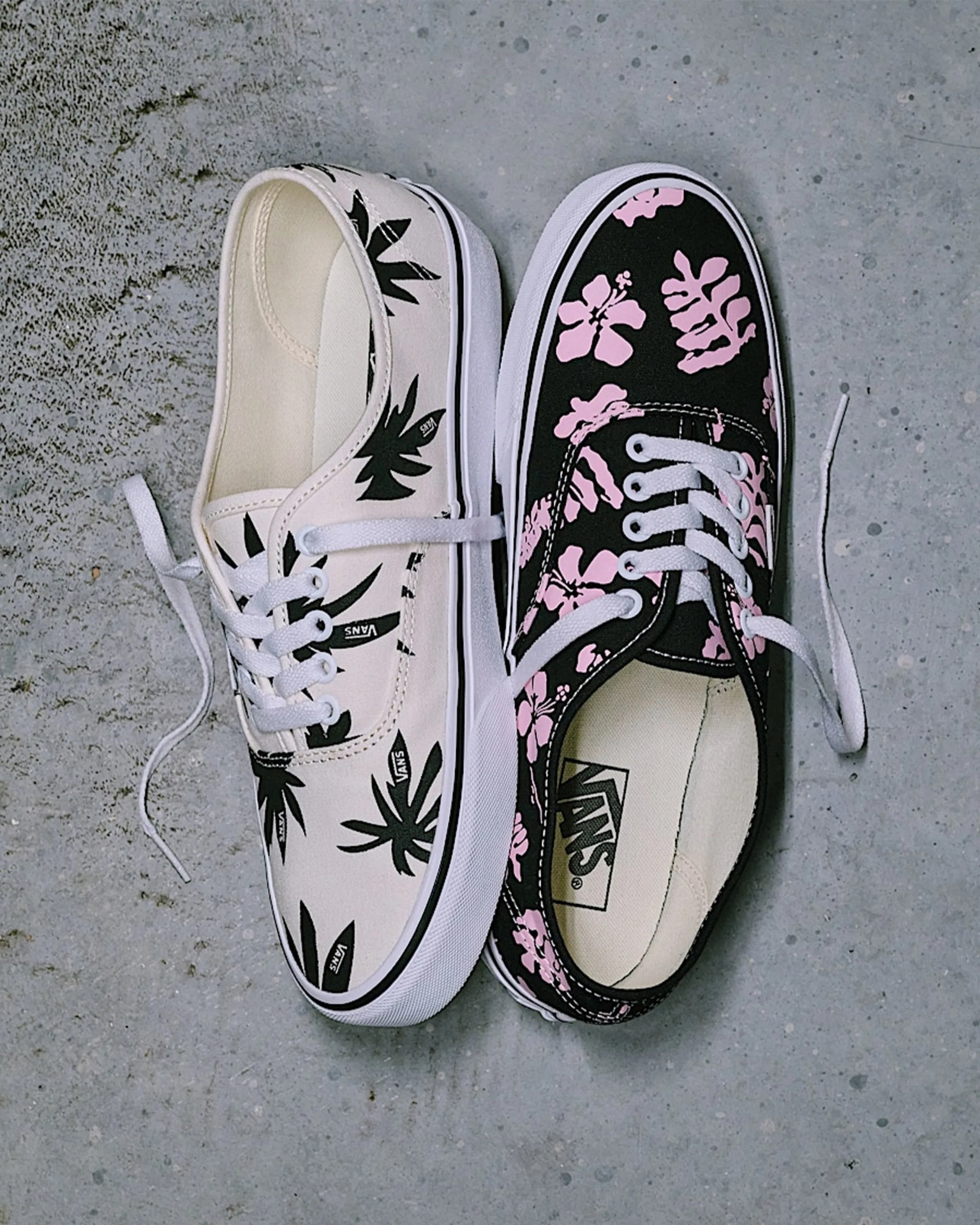 Pair of Vans sneakers with floral patterns, one white with black leaves and one black with pink flowers, on a concrete floor.