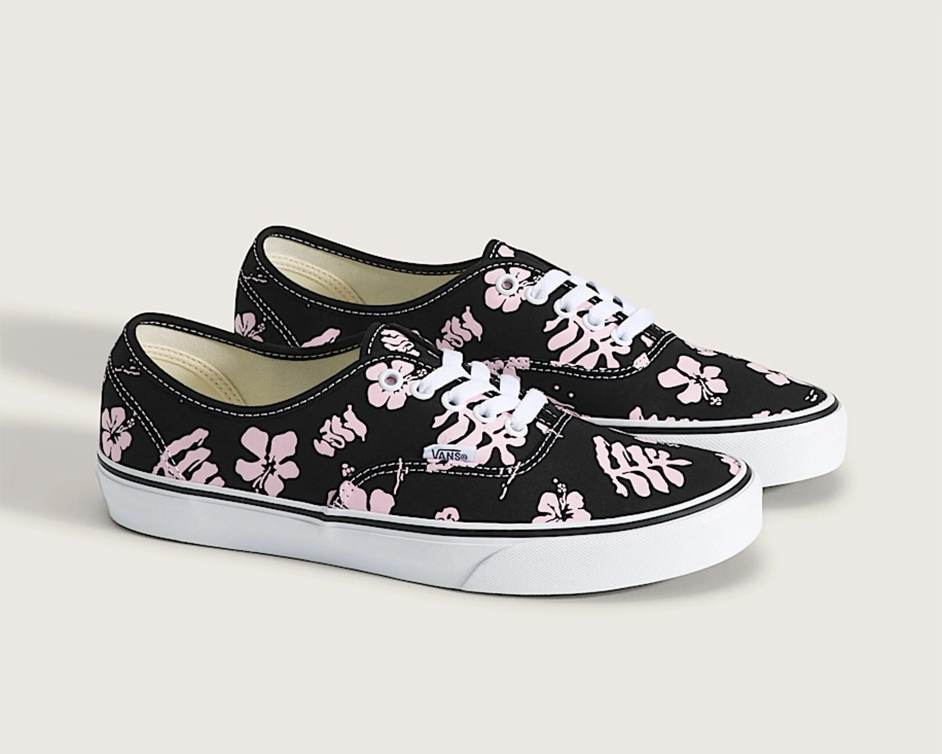 Pair of black Vans sneakers with pink floral print and white rubber soles on a light background.