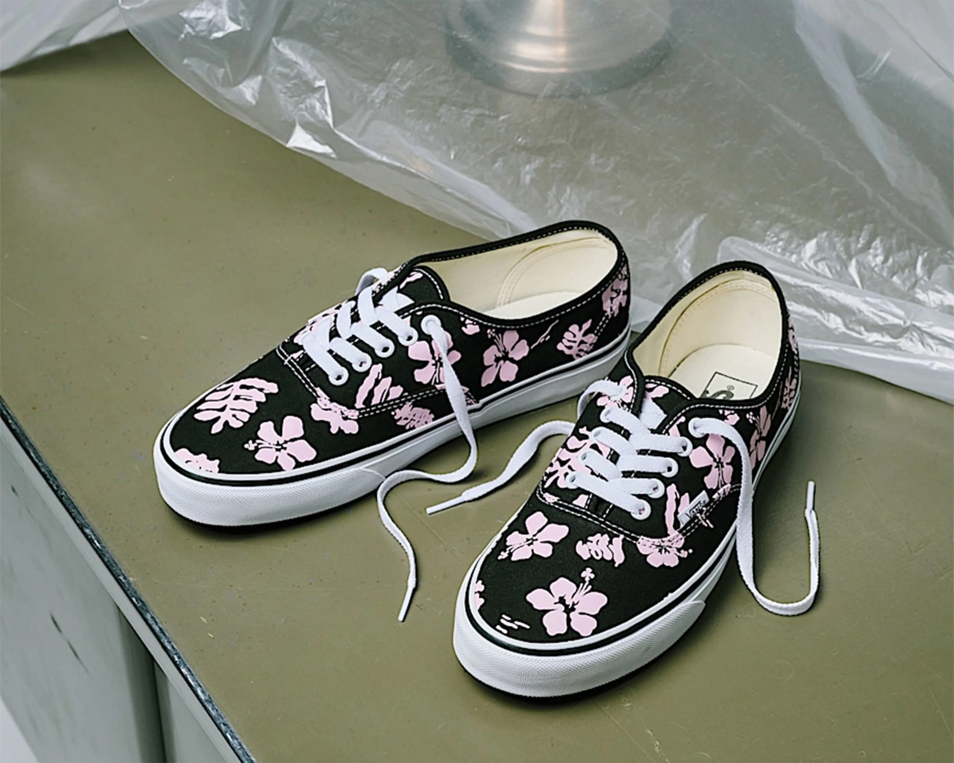 Pair of black canvas sneakers with pink floral print and white laces on a green surface.