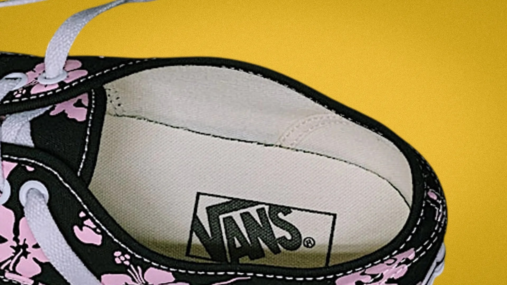 Close-up of the inside of a black Vans shoe with pink floral pattern and white laces on a yellow background.